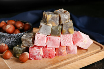 Wooden board with Turkish delight and hazelnuts on dark background