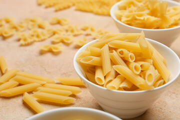 Bowl with uncooked penne pasta on color background