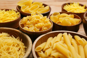 Bowls with different types of uncooked pasta on wooden background