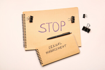 Notebooks with text STOP SEXUAL HARASSMENT and paper clips on color background