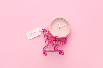 Alarm clock in small shopping cart on pink background, top view