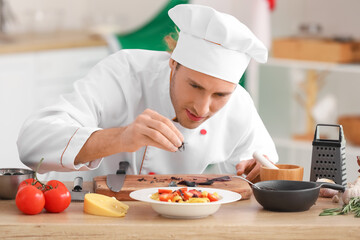 Italian chef putting basil onto plate with delicious pasta in kitchen