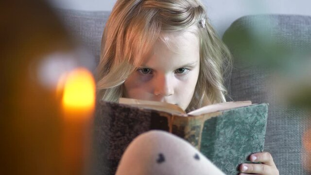 Close up of beautiful caucasian little girl reading book on sofa. Static view
