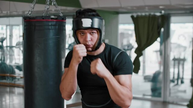 Young man boxer in soft protective helmet performing shadow boxing to a camera