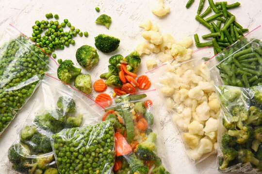 Plastic bags with different frozen vegetables on light background