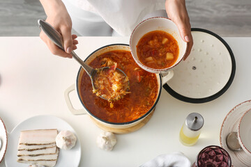Woman pouring delicious borscht from cooking pot to bowl, closeup