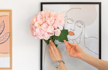 Woman with hydrangea flowers near picture in room