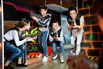 Fototapeta na wymiar Modern pleasant positive young people with laser pistols playing laser tag on dark labyrinth