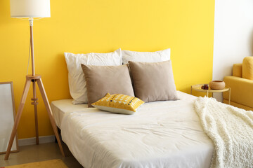 Comfortable bed and floor lamp near color wall