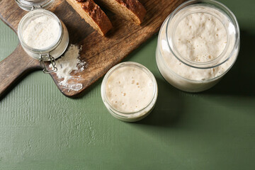 Jars with fresh sourdough on green wooden background