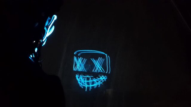 Neon mask with glow, boy with hood, reflection on the glass, mirror effect. Halloween and horror concept.