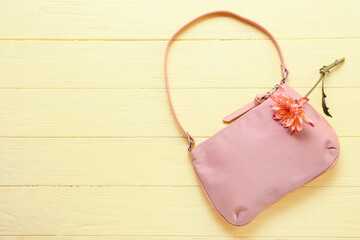 Stylish handbag and flower on color wooden background