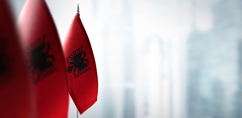 Small flags of Albania on a blurry background of the city - obrazy, fototapety, plakaty