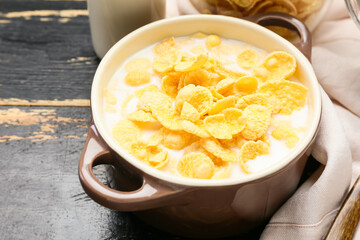 Pot of tasty cornflakes with milk on dark wooden background, closeup