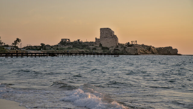 The coastal Crusader fortress of Ch&acirc;teau P&egrave;lerin (Atlit Castle), crashing Mediterranean Sea waves and fisherman dock in orange sunset in Atlit beach, Israel