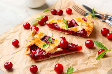 Parchment with pieces of tasty cherry pie on light background, closeup