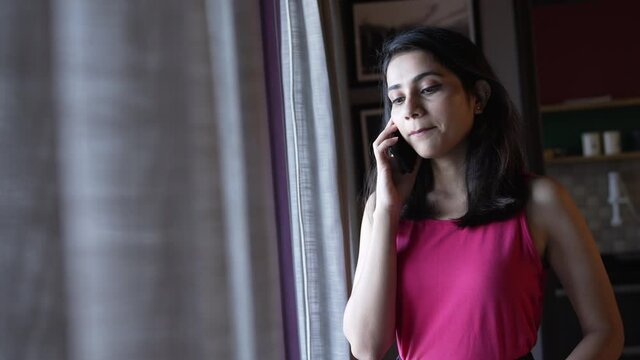 Portrait of Indain woman talking seriously  on smartphone with her family and friends.Closeup shot of a beautiful Asian girl  talking on mobile while standing near a window.