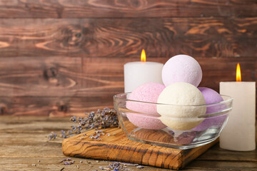 Bowl with lavender bath bombs and burning candles on wooden background