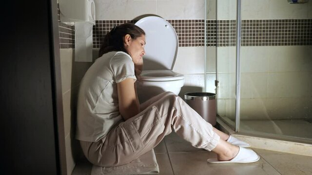 Young woman sitting near toilet, poisoning, toxicosis.