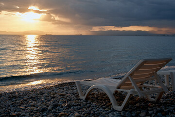 Fototapeta na wymiar Beautiful sunset, one sun lounger. Pebbles, sea view with horizon, colorful twilight sky, tranquility and relaxation. Greece. 