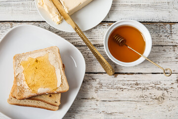 Plate of tasty toasted bread with honey and butter on white wooden background