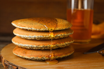 Wooden board of tasty pancakes with honey on table, closeup