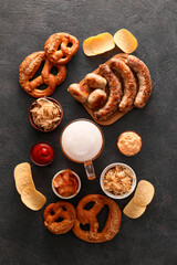 Mug of cold beer, wooden board with Bavarian sausages and snacks on black background. Oktoberfest celebration