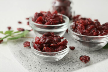 Bowls with tasty dried cranberries on light background, closeup