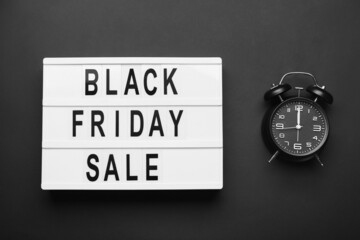 Board with text BLACK FRIDAY SALE and clock on dark background