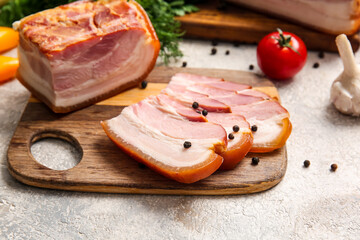 Wooden board with tasty smoked bacon on light background