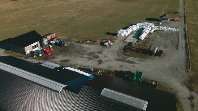 Stack Of Wrapped Silage Bales And Dairy Farm Equipment Outside A Barn. Dairy Milk Industry In Norway. aerial orbit