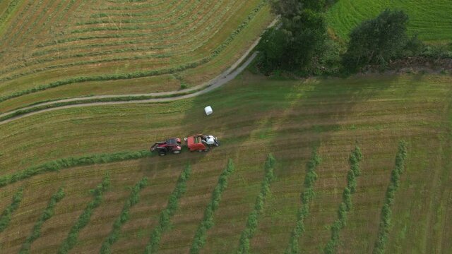 Silage Bale Wrapper And Grass Turner Farm Machinery At Work On Farmland, Norway. aerial