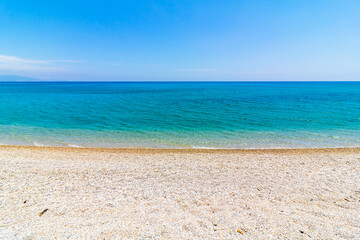 Fototapeta na wymiar Pebbles on the beach and turquoise sea against clear blue sky. Summer background