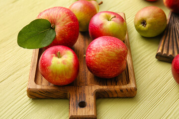 Wooden board with ripe apples and pear on color wooden background