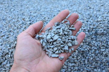 man holds in his hand a sample of stone gravel or pebbles of one size. Marble white gravel and gray...