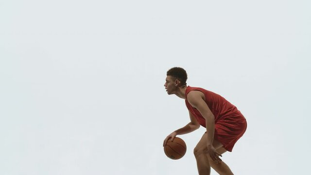 Guy basketball player dribbling ball, hitting it on floor and throws into basket. Young athlete trains before streetball competition. Picture taken in the studio on a white background in slow motion.