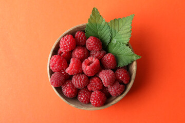 Red juicy raspberries in a wooden bowl on an orange background.
