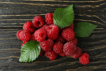 Handful of raspberries with leaves on wooden background