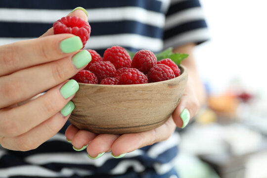 Woman holding wooden bowl with raspberries, cloce up