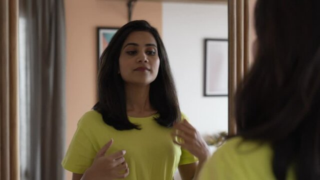 Indian woman curling hair with hair curler fashion with herself in front of mirror in bedroom.Happy beautiful young asian woman styling shot hair looking in front of mirror at bedroom in the morning. 