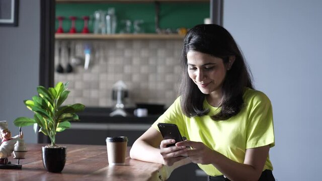 young Indian woman siting on a table and use mobile phone for communication.Portrait of a Asian smiling girl sitting on office desk and texting message on mobile phone.