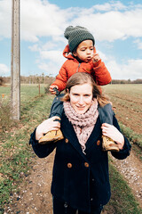 happy single mom with her adopted son on shoulders walking in the countryside - focus on hood child...