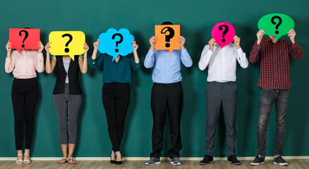 group of people holding speech bubble card with question mark sign in front of their faces. Standing isolated in front of green background
