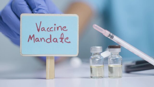 Concept of coronavirus or covid-19 vaccine mandate, showing with doctor hands with gloves by placing sign board next to vaccine shots and syringe.
