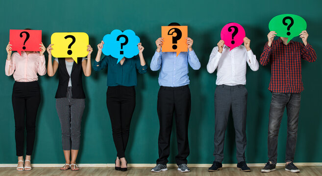 Group Of People Holding Speech Bubble Card With Question Mark Sign In Front Of Their Faces. Standing Isolated In Front Of Green Background