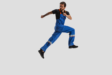 Fototapeta na wymiar Portrait of young man, male auto mechanic in dungarees running isolated over white studio background. Concept of labor, occupation, funny meme emotions