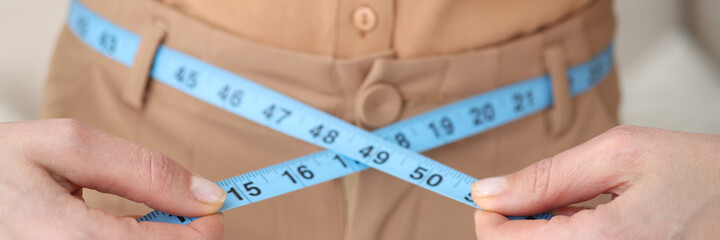 Woman measures her waist with centimeter closeup