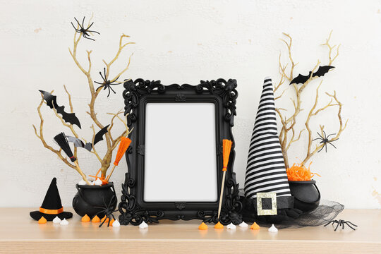 holidays image of Halloween. witcher cauldron and hat, broom, bare trees, photo frame over white wooden table
