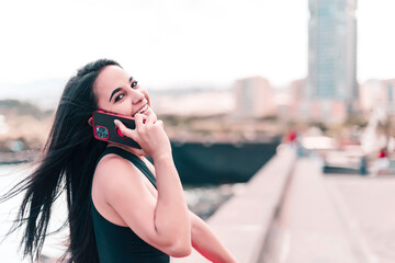 Close up portrait of young woman who's talking by phone and smiling in the city street. In a distance connecting concept