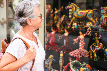 Smiling traveler senior woman visiting Barcelona, looking artistic creations in a shop window. Happy retired enjoying vacations